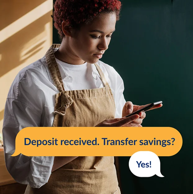 Person using a mobile phone with messaging that reads, “Deposit received. Transfer savings? Yes!”